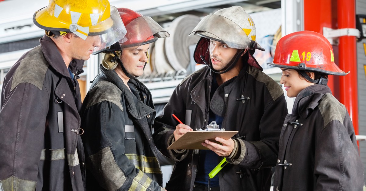 A group of firefighters huddled together with one firefighter holding a clipboard and a pen.