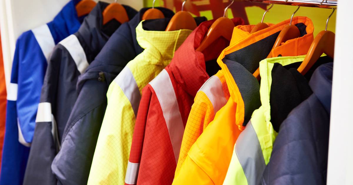 Nine fire-resistant industrial work coats in various colors, designed for safety and durability, hang neatly on a rack.