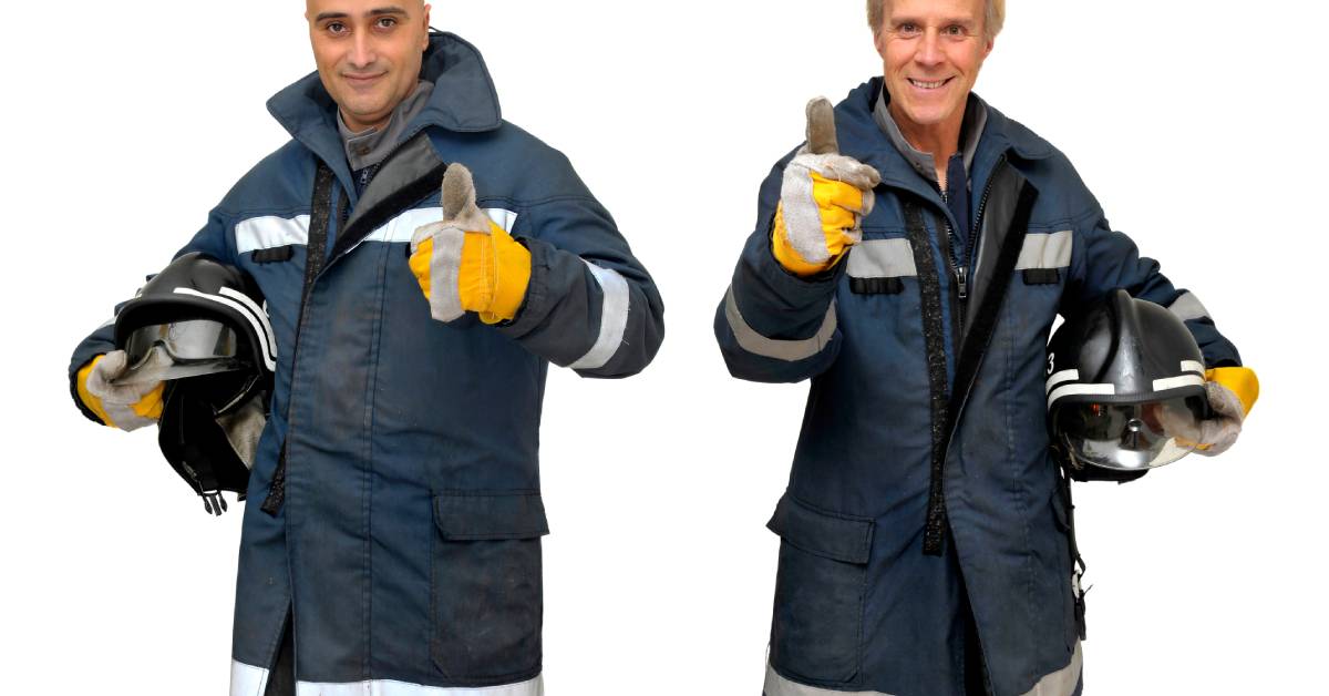 Two firemen standing together wearing fire-resistant gear in front a white background giving a thumbs-up.