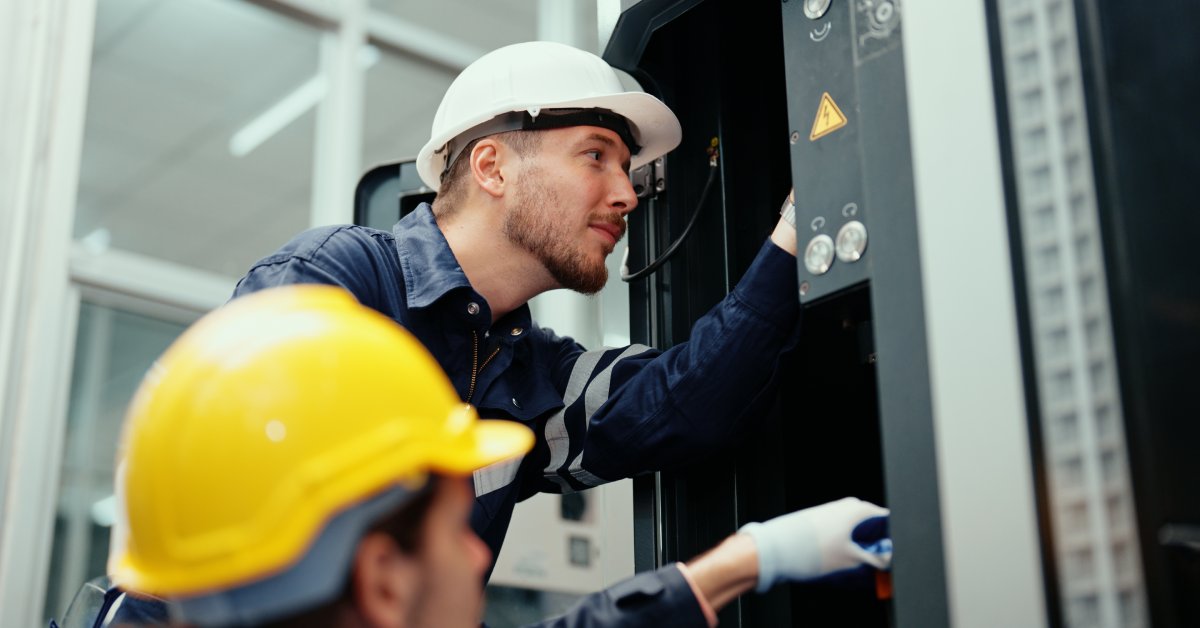 A worker in a white hard hat and a worker in a yellow hard hat wear protective FR clothing while working.